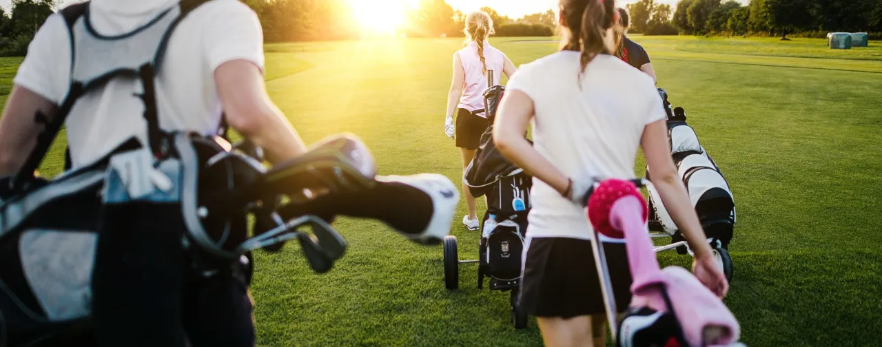 Fyra personer bär golfklubbor på en golfbana.