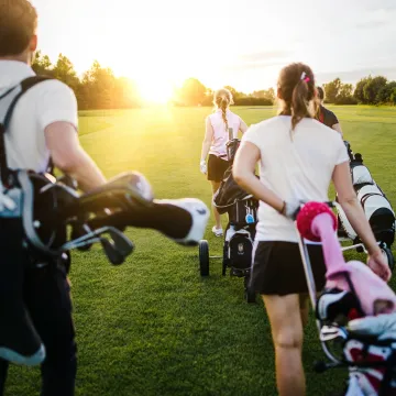 Fyra personer bär golfklubbor på en golfbana.