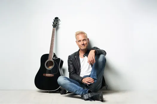 Thomas Järvheden sitter på golvet med en gitarr bredvid sig.