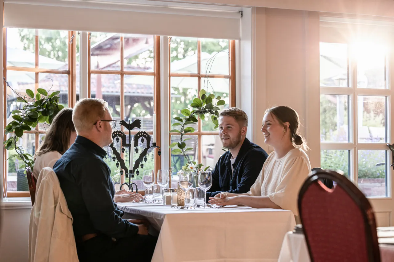 Fyra personer sitter vid ett dukat bord och samtalar.